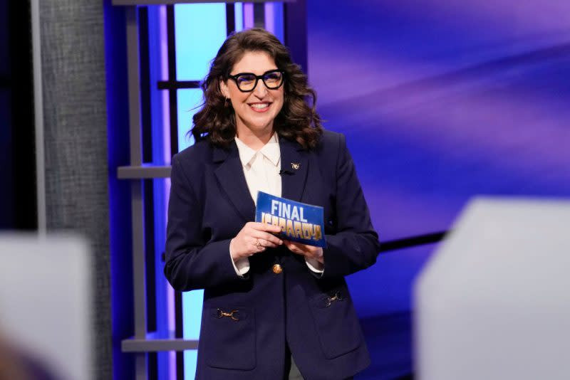 Mayim Bialik on the Jeopardy! set during the National College Championship in 2022, smiling and looking towards the game board.