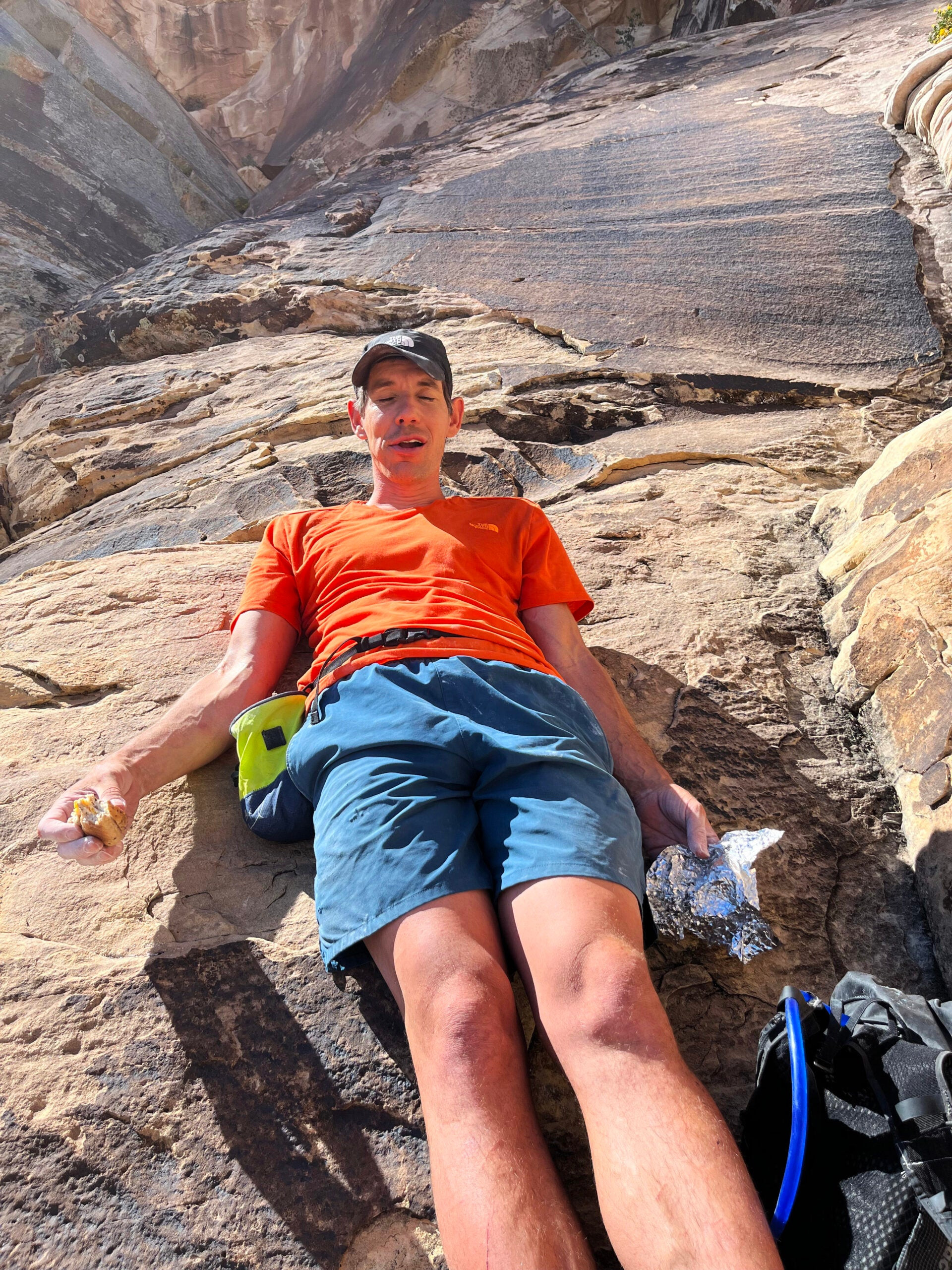 Alex Honnold looking exhausted, eating with his eyes closed, below Epinephrine