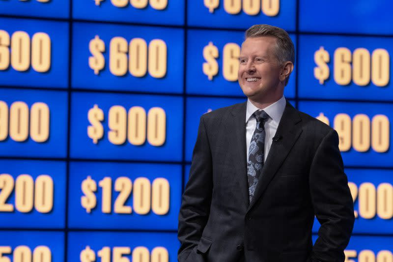 Ken Jennings during a taping of Celebrity Jeopardy! in 2023, pointing at the game board with a pen and smiling.