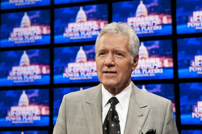 Alex Trebek smiling warmly during a Jeopardy! rehearsal in 2012, wearing a suit and tie and standing on the Jeopardy! stage.